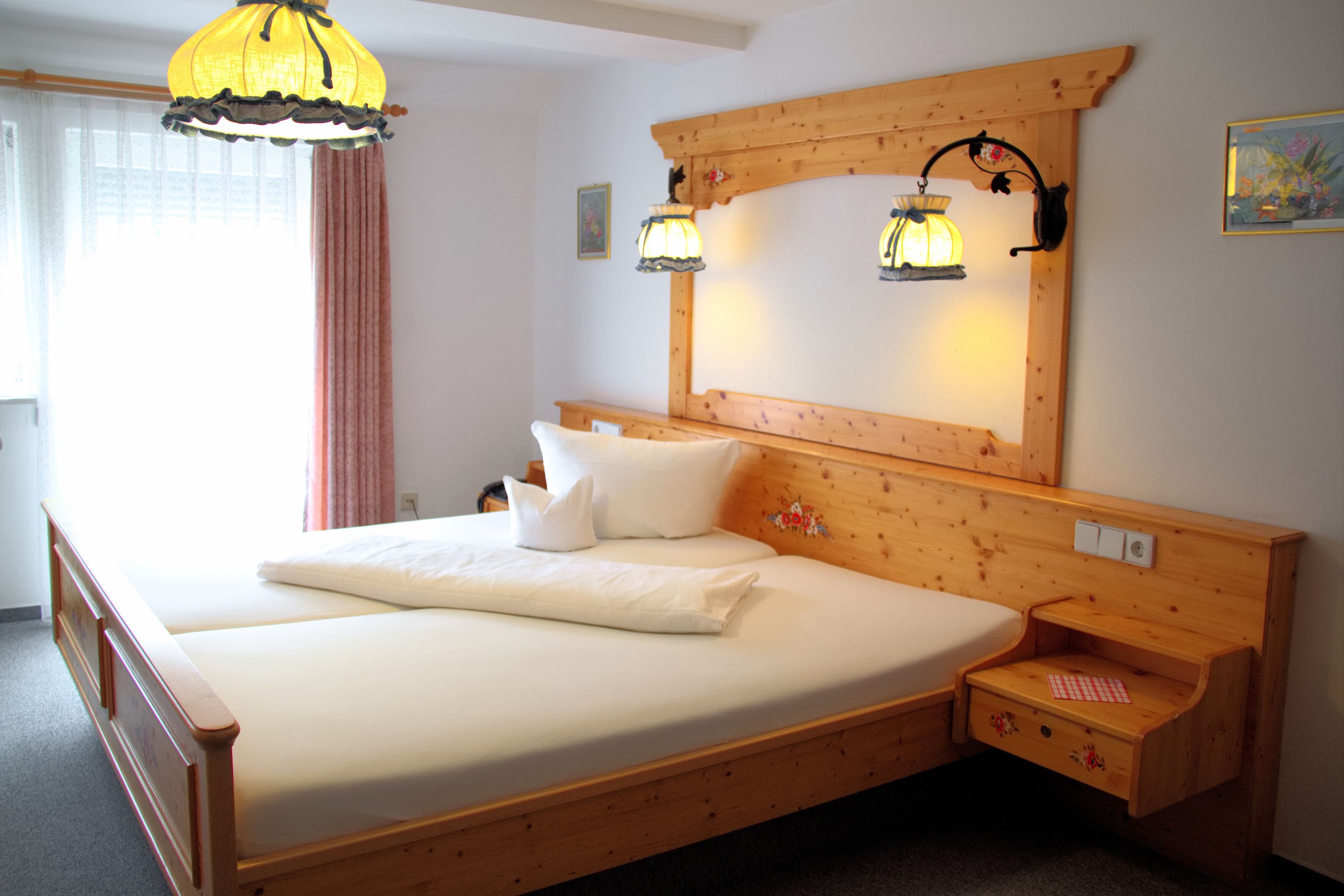 A wooden bed with a headboard, two bedside lamps, and a nightstand.