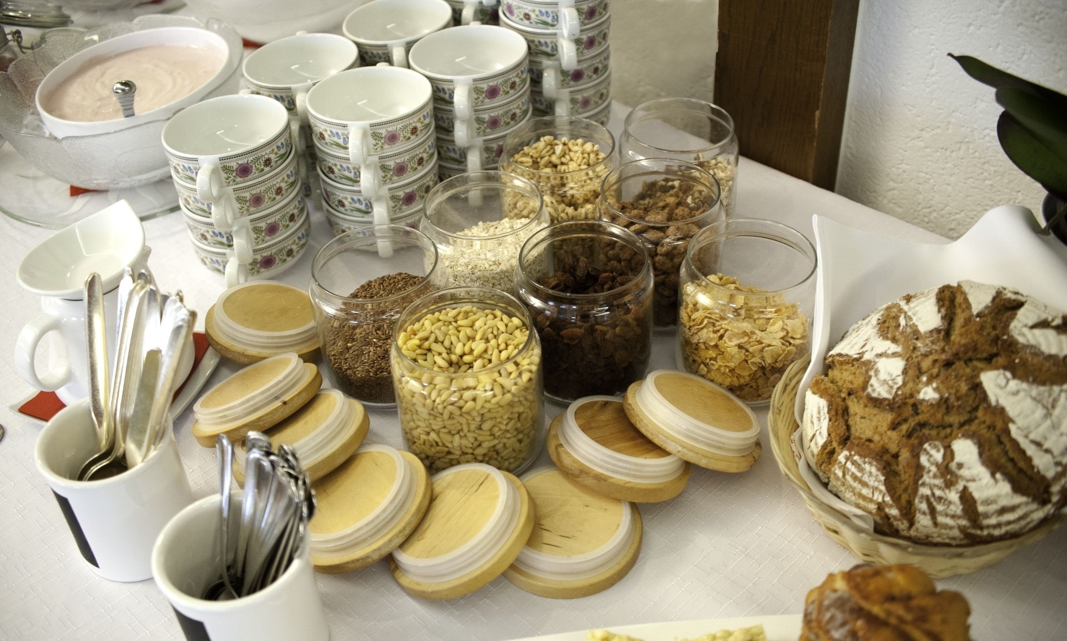 A table with various food items and utensils, including jars of grains and a loaf of bread.