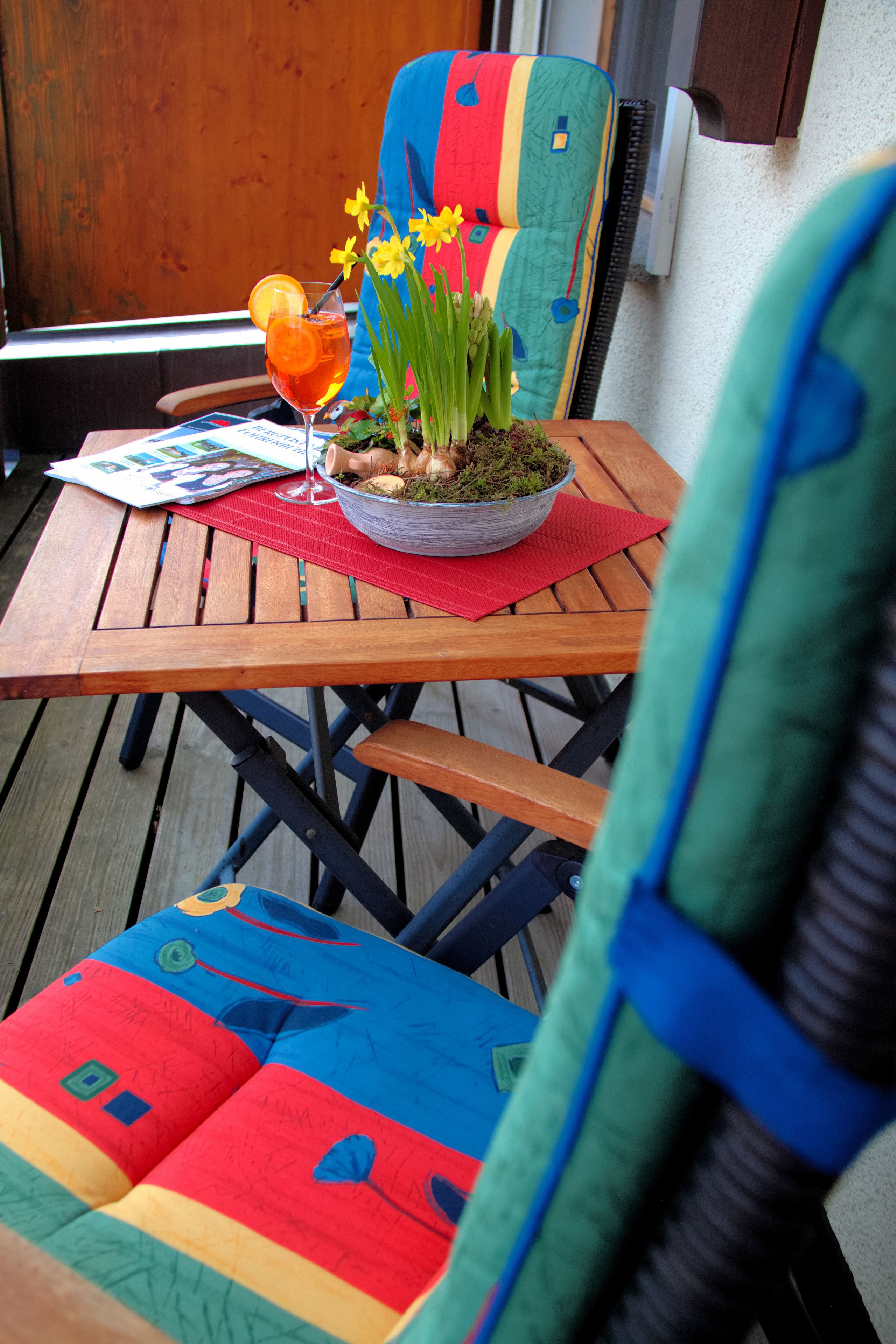 Een houten tafel met een kleurrijke stoel, een glas drinken en een schaal met bloemen.