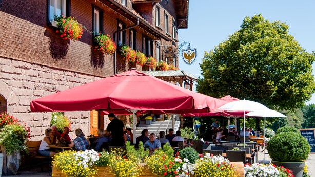 An outdoor seating area with red umbrellas, brick building, and flower boxes on the windows.