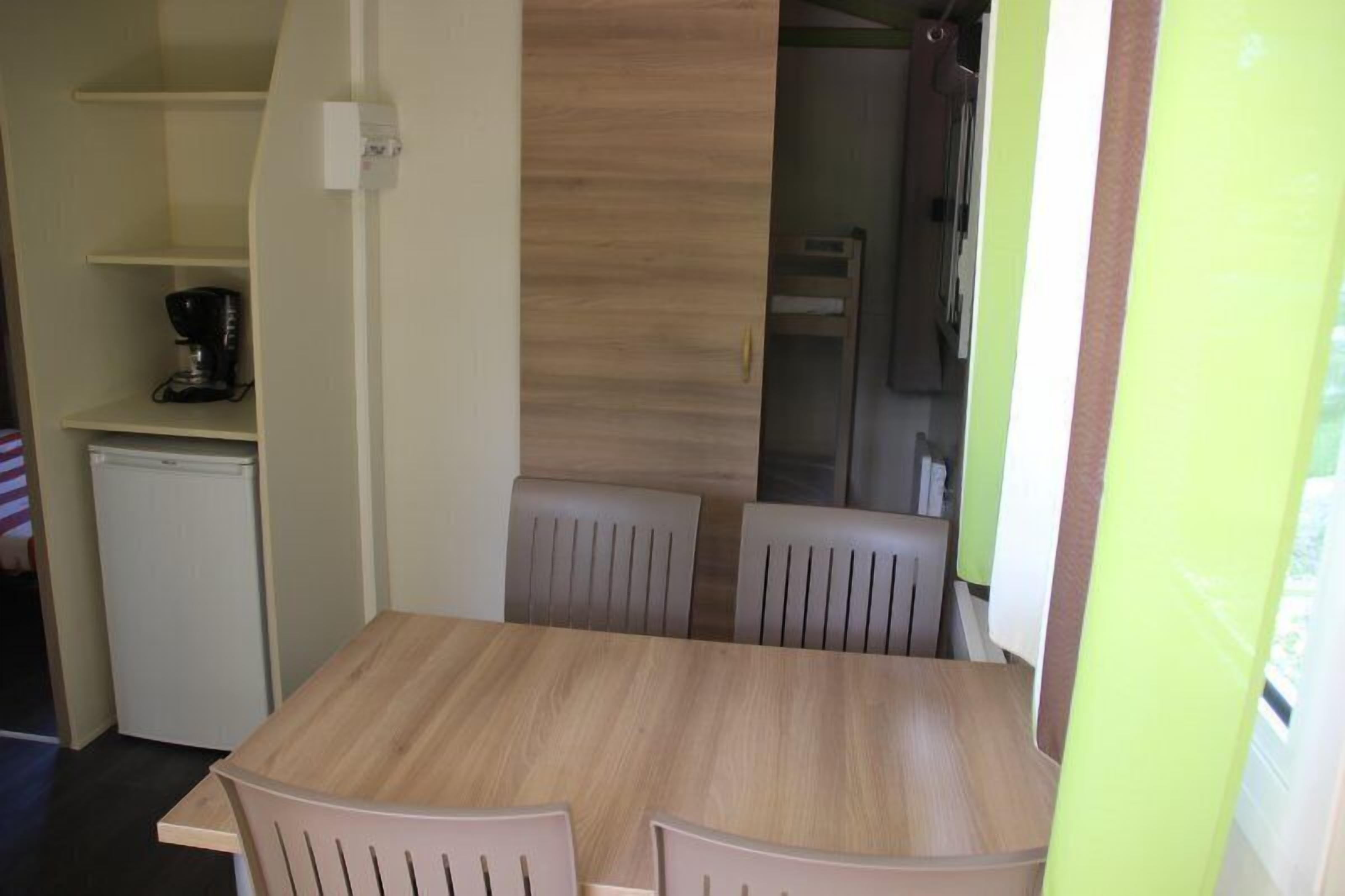 Een compact keukenhoekje met een koffiezetapparaat, een kleine koelkast en een houten tafel met stoelen.