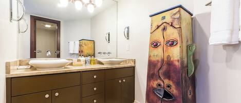 A bathroom with a double sink vanity, a large mirror, and a unique cabinet with a face painted on it.