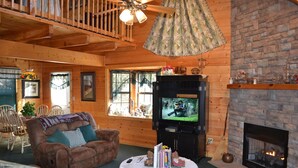 A cozy log cabin interior with a fireplace, a television, and a comfortable seating area.