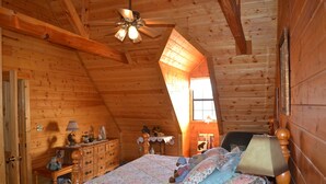 A wooden cabin bedroom with a bed, dresser, and a ceiling fan.
