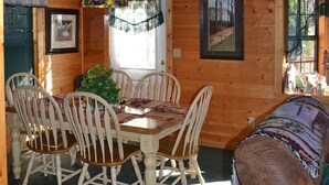 A wooden cabin interior with a dining table, chairs, a sofa, and a hanging light fixture.