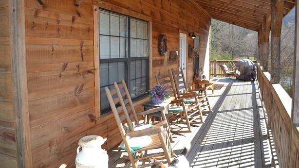 A wooden cabin with a porch, wooden chairs, a table, and a window.