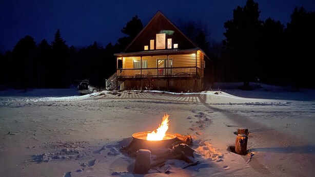 A log cabin with a fire pit in the foreground, surrounded by snow. - Quiet, Private and Comfortable  nestled on 8 acres of private property    (Lead)