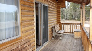 A wooden cabin with a covered porch, a sliding glass door, and a bench. - Quiet, Private and Comfortable  nestled on 8 acres of private property    (Lead)