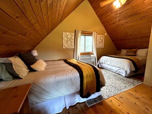 A cozy attic bedroom with two beds, a window with curtains, and wooden walls. - Quiet, Private and Comfortable nestled on 8 acres of private property (Lead)