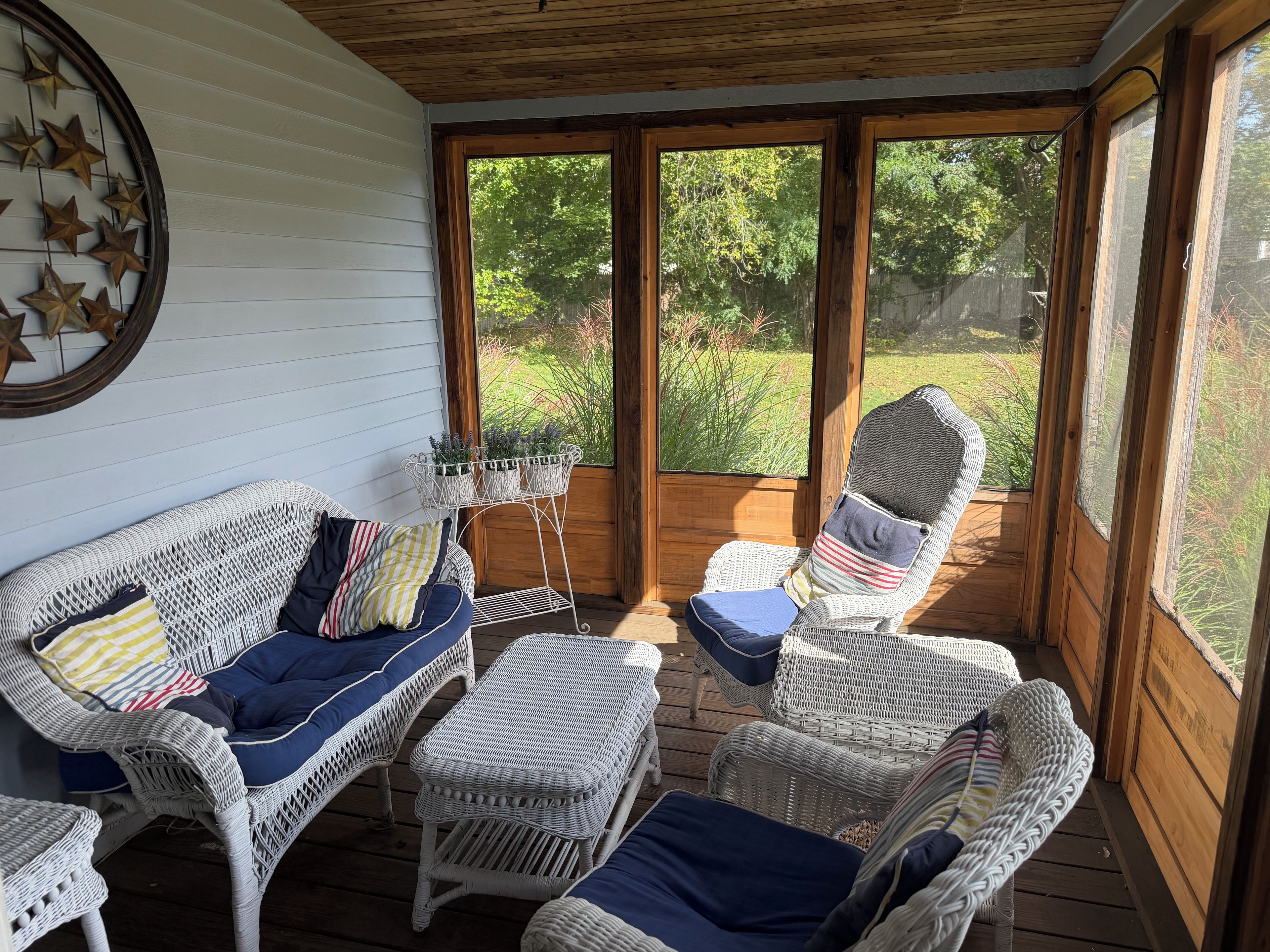 A covered porch with wicker furniture, a star wall decoration, and a view of a garden.