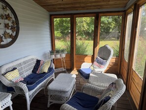 A covered porch with wicker furniture, a star wall decoration, and a view of a garden.