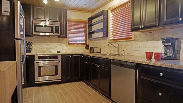 A modern kitchen with stainless steel appliances, dark cabinetry, and a tiled backsplash.
