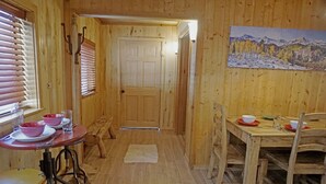 A wooden interior with a dining table set for two, a bench, and a door leading to another room.