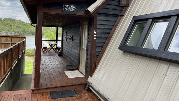 A wooden deck with a covered area, a sign reading "Lake Side Paradise," and a view of a lake. - OVERSIZED PORCH, LAKE FRONT, Mammoth Cave, Fast WiFi, Firepit, hiking (Mammoth Cave)