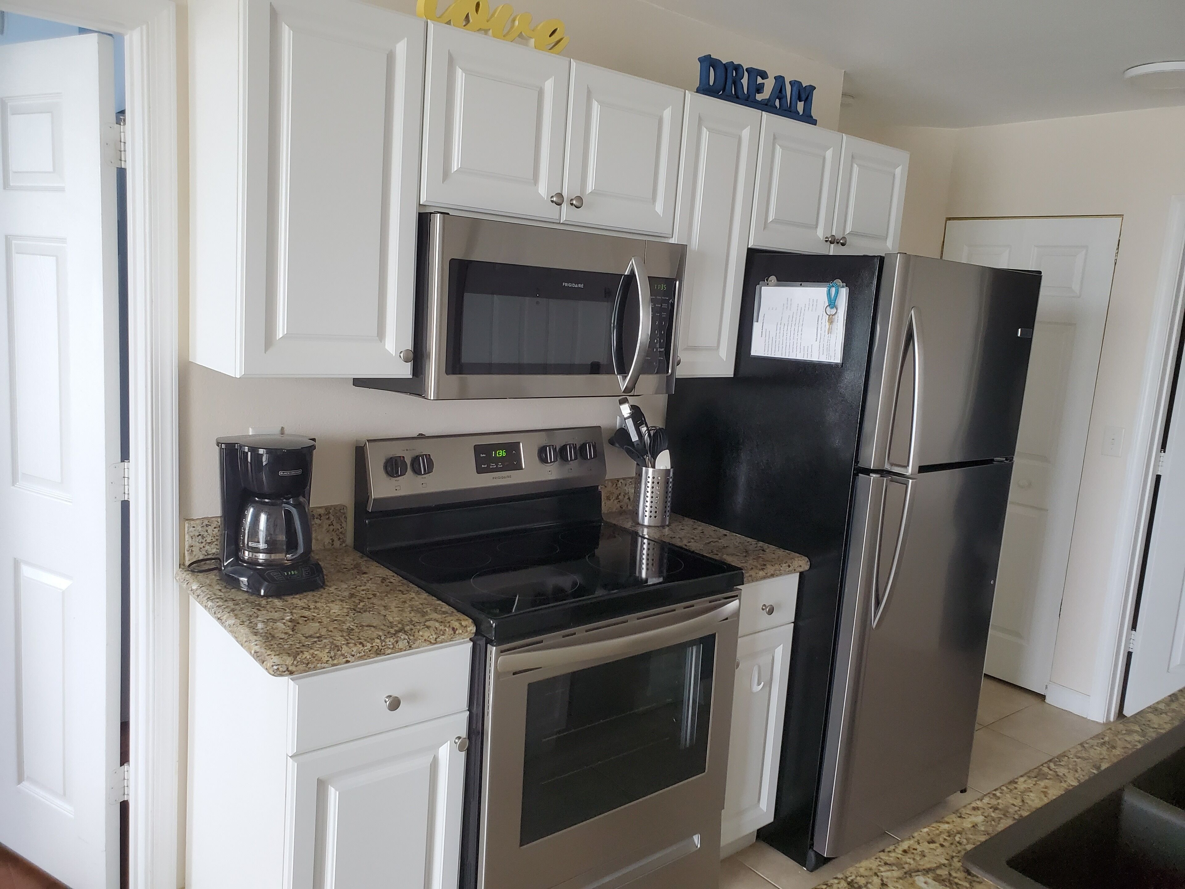 A modern kitchen with white cabinetry, a stainless steel refrigerator, a microwave, a coffee maker, and a stove.