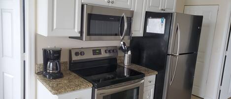 A modern kitchen with white cabinetry, a stainless steel refrigerator, a microwave, a coffee maker, and a stove.