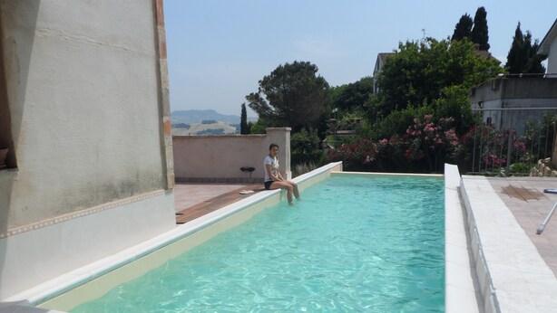 Ein Schwimmbad mit klarem Wasser, eine Person sitzt am Beckenrand, und im Hintergrund ist die Landschaft zu sehen.