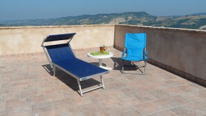Eine Dachterrasse mit einem blauen Liegestuhl, einem kleinen Stuhl und einem Tisch mit Getränk und Speisen.