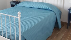 Ein Bett mit weißem Metallgestell und einer blauen, gesteppten Bettdecke.