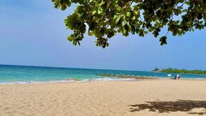 A sandy beach with clear blue water and a few people in the distance. - Spacious 5 Bedroom Villa, Centrally Located, Near Beach. (Runaway Bay)
