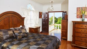 A bedroom with a large bed, wooden dresser, and a view of greenery outside. - Spacious 5 Bedroom Villa, Centrally Located, Near Beach. (Runaway Bay)