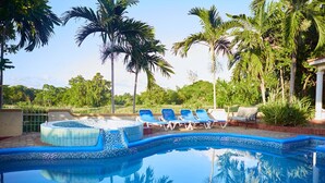 A swimming pool with blue tiles, surrounded by palm trees and lounge chairs. - Spacious 5 Bedroom Villa, Centrally Located, Near Beach. (Runaway Bay)