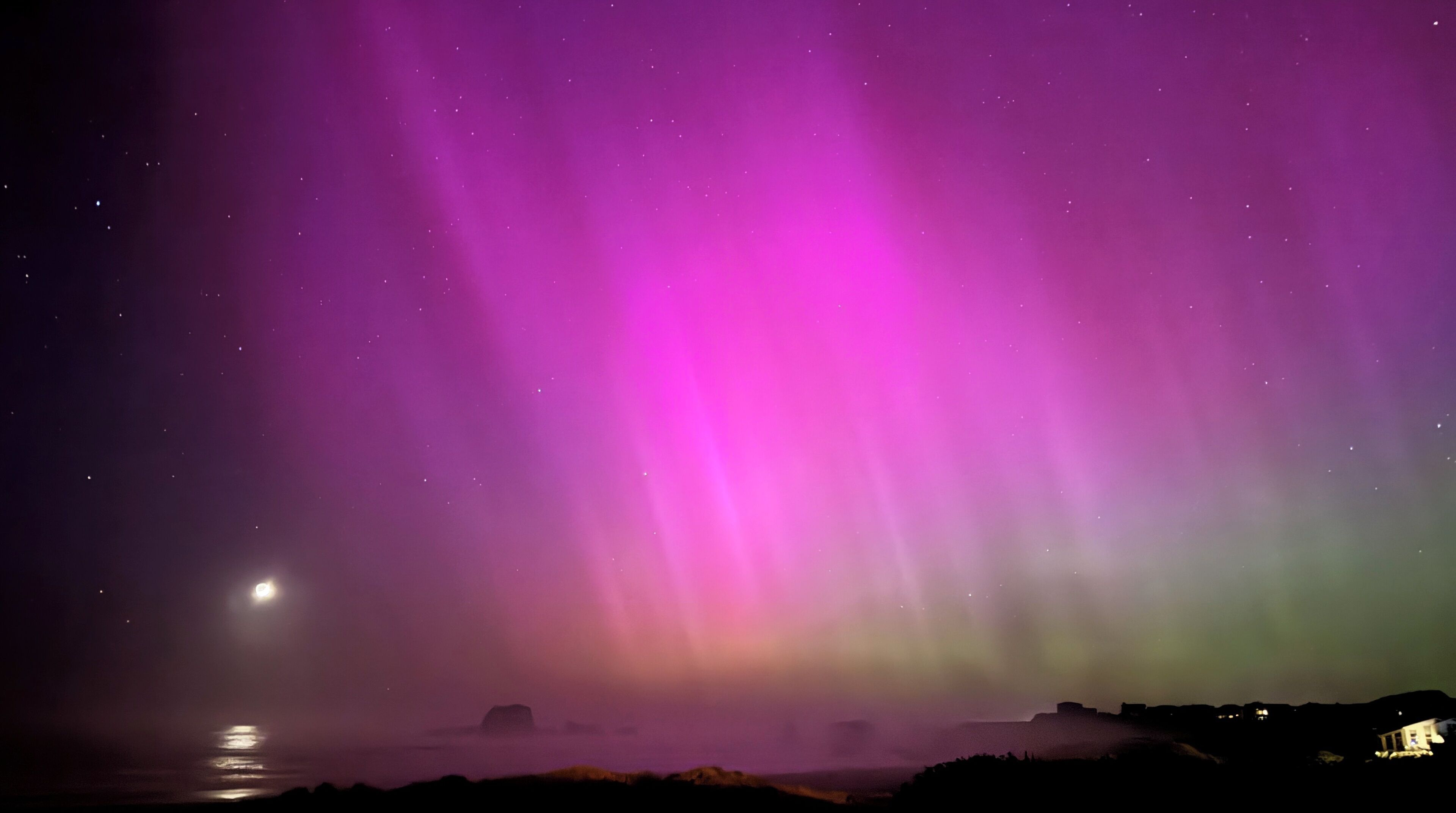 Un ciel nocturne illuminé par des aurores boréales, au-dessus d’un paysage côtier.