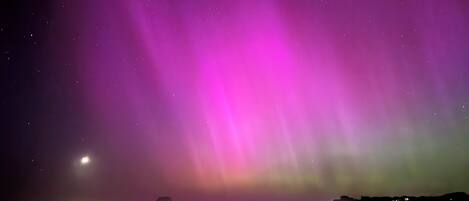 Un ciel nocturne illuminé par des aurores boréales, au-dessus d’un paysage côtier.