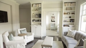 Een woonkamer met witte meubels, een boekenkast en een televisie.