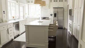 Een moderne keuken met witte kasten, een centraal eiland, roestvrijstalen apparatuur en hanglampen.
