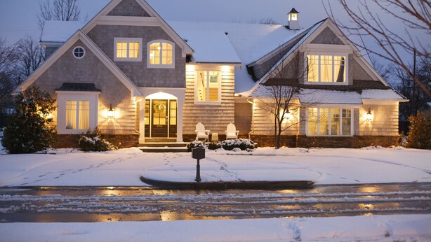 Een huis met twee verdiepingen, een sneeuw bedekte oprit en een klein vijvertje op de voorgrond.