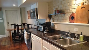 A kitchen with a granite countertop, stainless steel sink, and white cabinetry. - The Garden Apartment with a Murphy Table (Savannah)