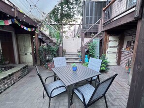 An outdoor patio with a wooden table and chairs, surrounded by potted plants and a brick wall.