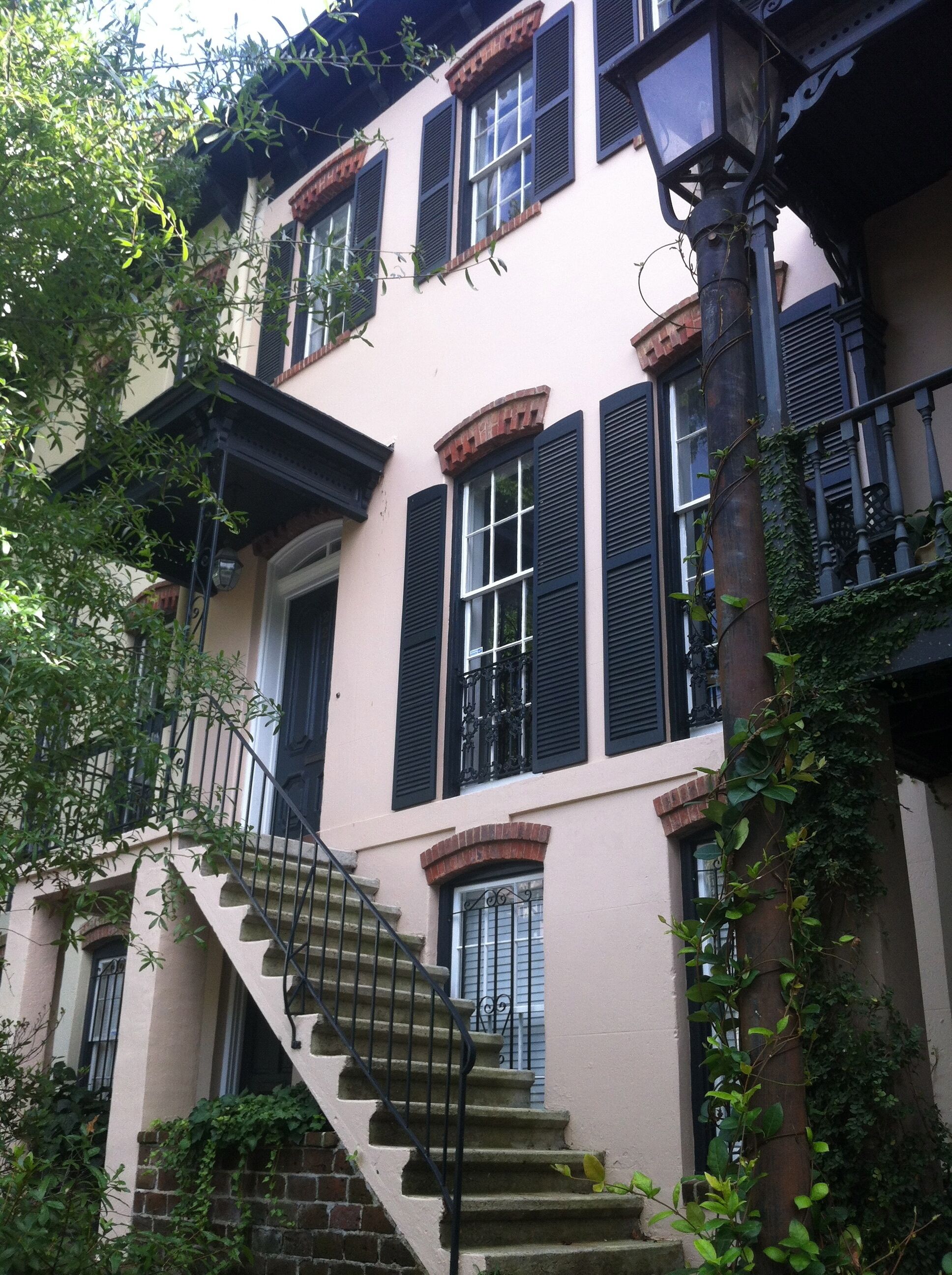 Un immeuble à plusieurs étages, doté d’une façade en briques, de volets noirs et d’un escalier central menant à l’entrée.