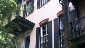 A multi-story building with a brick facade, black shutters, and a central staircase leading to the entrance. - The Garden Apartment with a Murphy Table (Savannah)