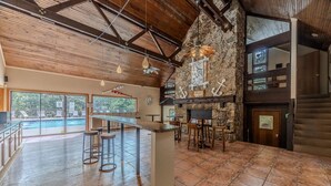 A bar area with stools, a stone wall, and a view of a pool. - 22 Mile Marker! Indoor/Outdoor Pools, Hot Tub! New (Osage Beach)