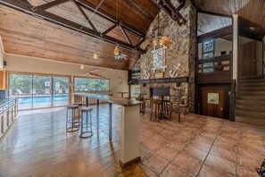 A bar area with stools, a stone wall, and a view of a pool.