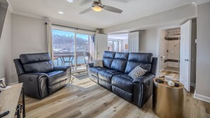 A modern living room with a leather sofa and armchair, a ceiling fan, and a view through a sliding glass door. - 22 Mile Marker! Indoor/Outdoor Pools, Hot Tub! New (Osage Beach)