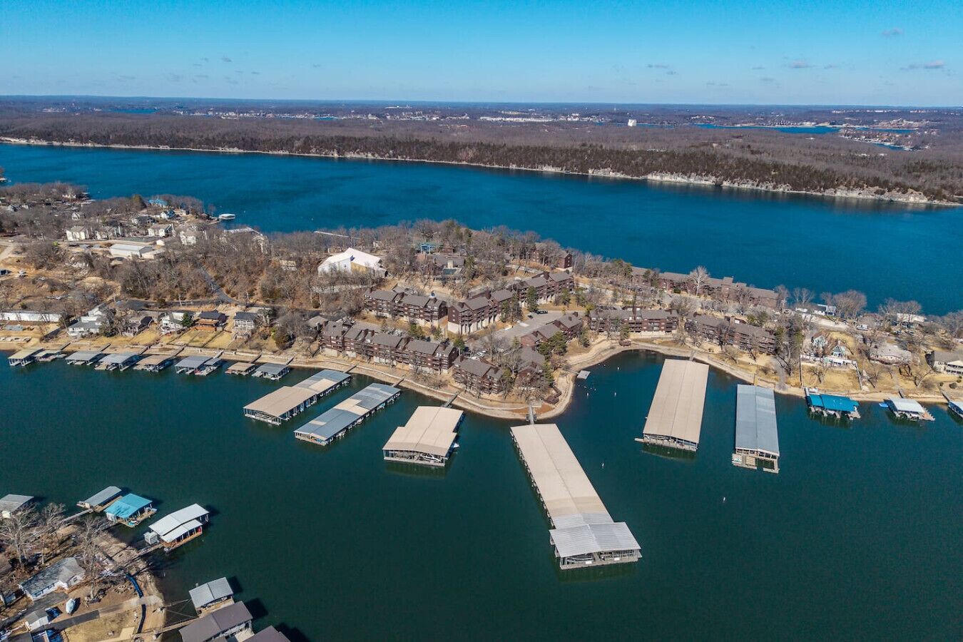 An aerial view of a lakeside property with docked boats, a marina, and residential buildings.