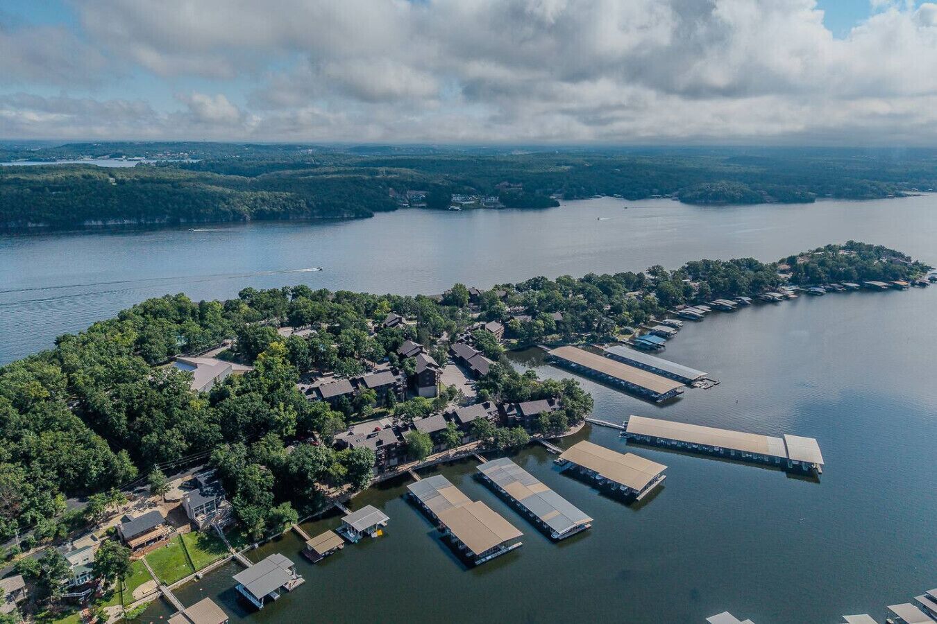 Vista aérea de una propiedad junto al lago con barcos amarrados, un puerto deportivo y edificios residenciales rodeados de vegetación.