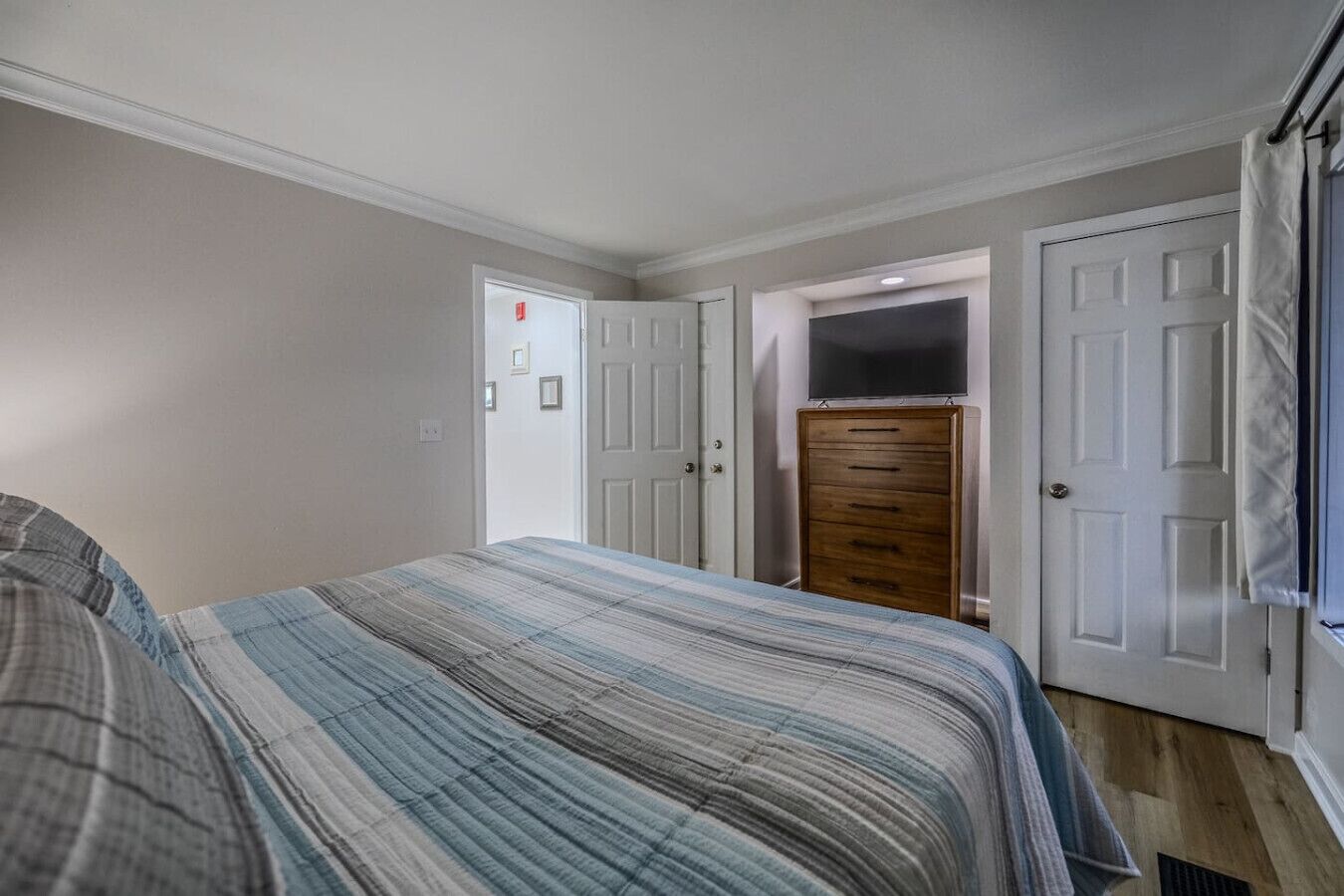A bedroom with a bed, a dresser, and a door leading to another room.