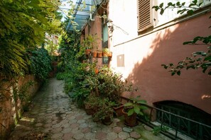 A narrow cobblestone alley with potted plants and a metal fence.
