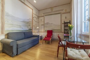 A living room with a blue sofa, a red armchair, a glass coffee table, and a bookshelf.
