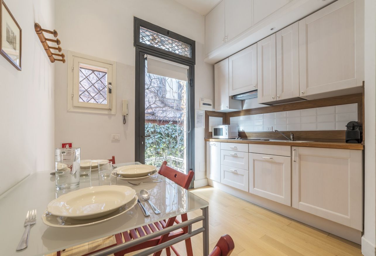Una cocina moderna con armarios blancos, encimera de madera y zona de comedor con mesa y sillas de vidrio.