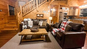 A cozy cabin interior with a wooden staircase, a leather sofa, a dining table, and a kitchen area. - *Beautiful Cabin With Gorgeous Views and Privacy*-Sunset Ridge (Sevierville)