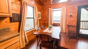 A wooden cabin interior with a dining table, chairs, a small plant, and a window with curtains. - *Beautiful Cabin With Gorgeous Views and Privacy*-Sunset Ridge (Sevierville)