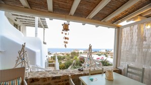 Una terraza con muro de piedra, mobiliario blanco y vista al mar y edificios.