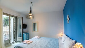 Un dormitorio con cama, mesita de noche, lámpara, ventana y puerta que da a un área exterior.