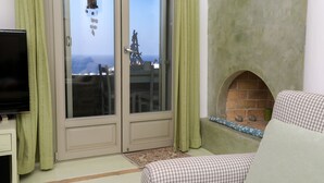 Una sala de estar con televisor, un sofá a cuadros, chimenea y vistas a través de un ventanal.