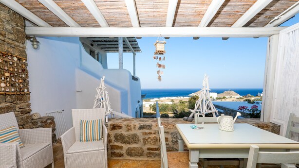 Una terraza con mobiliario de mimbre, un muro de piedra y vistas al mar.
